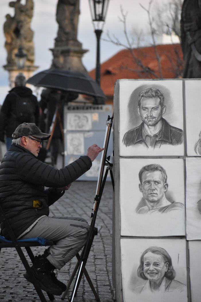 about-02 An outdoor artist sketches portraits on a street in Prague, capturing lively street art.