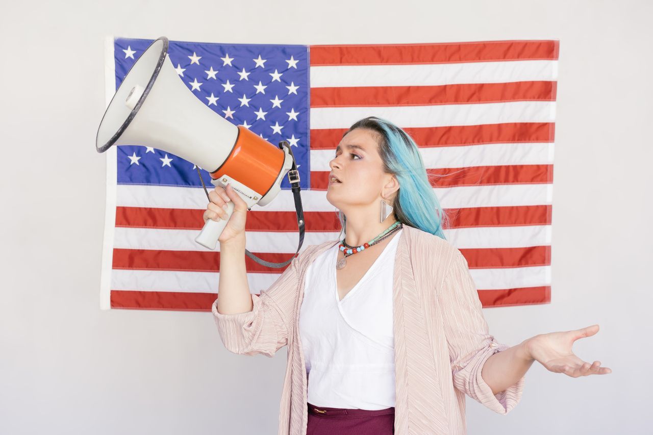 Confident woman with a megaphone in front of an American flag, expressing courage.