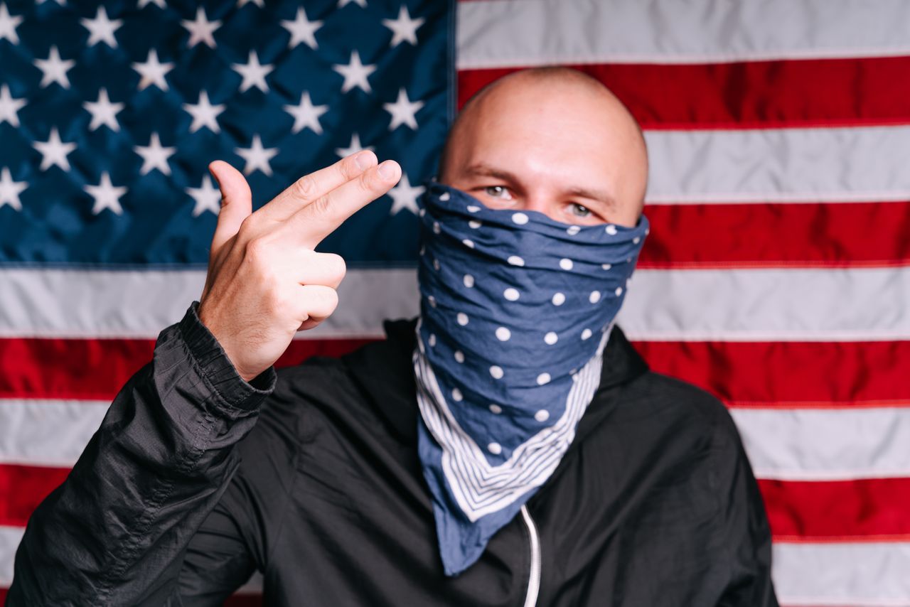 Man wearing a bandana making a hand gesture in front of the American flag.